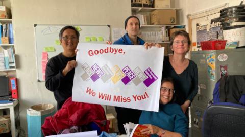 The PN staff, in the PN office, 5 Caledonian Road: (from left to right, standing) Milan Rai, Gabriel Carlyle and Emma Sangster plus (below, holding book) Emily Johns. (The poster was made for Claire Poyner when she retired as PN admin worker in 2023.) Photo: PN